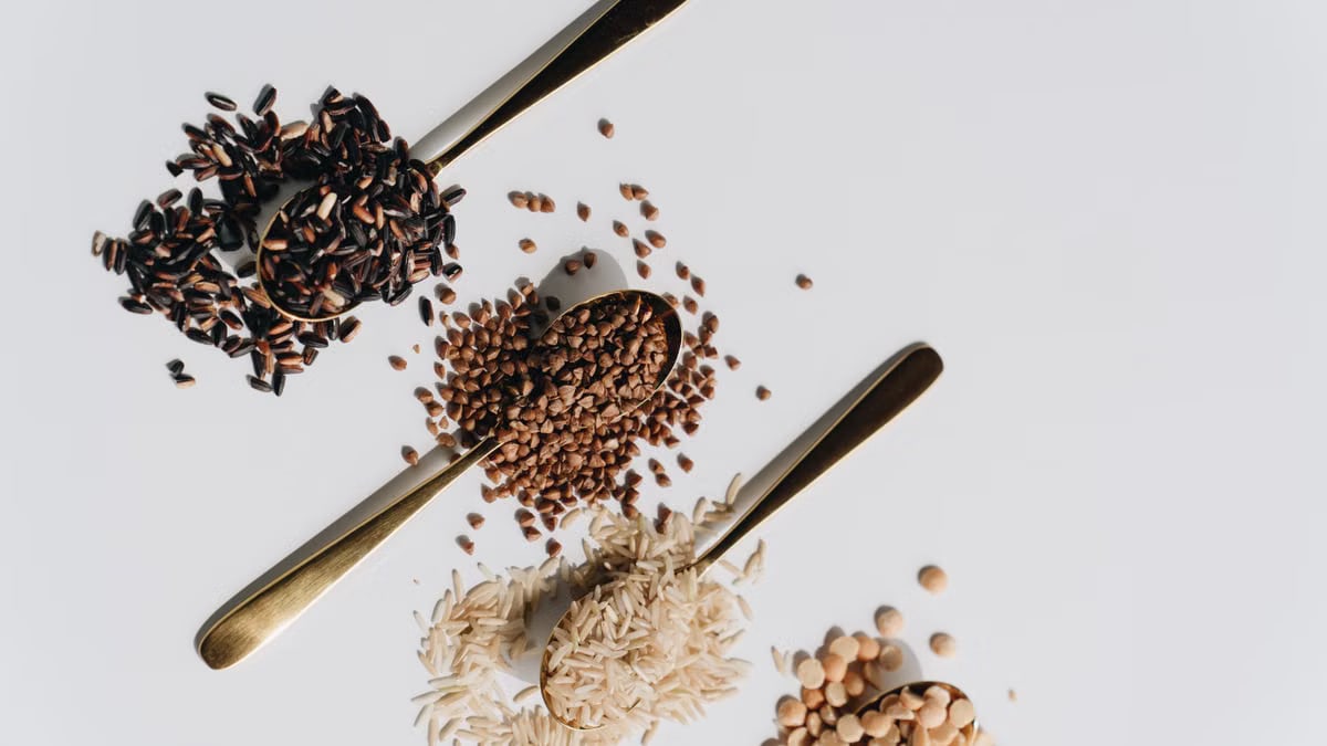 Top view of various dry grains on spoons against a white background, showcasing a variety of textures and colors.