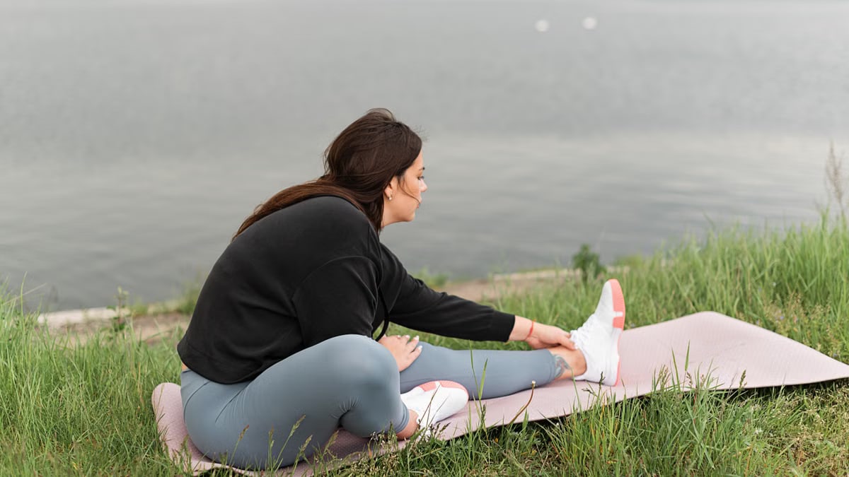 A woman stretches on a yoga mat by a serene lake, embodying relaxation and wellness in nature.